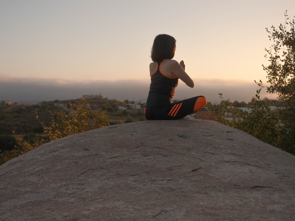 An image of a woman performing meditation on top of a rock